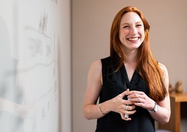 A lady in blue tank top standing next to a white board